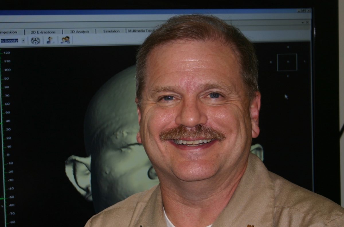 Gerald Thomas Grant in Navy uniform in front of a 3D facial scan on a workstation monitor